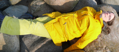 Das Foto zeigt mich, wie ich auf dem Rücken auf großen Steinen liege. Ich habe eine hellgrüne Hose an, eine gelbe lange Jacke, dunkelblondes Haar, die Augen geschlossen, ein Fast-Lächeln im Gesicht, hell-fastrosa Haut und eine Brille.