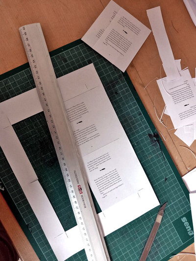 Aus einem A4-Papier sind zwei der vier A7-Seiten ausgeschnitten. Das Cutter-Messer, Stahllineal und bereits ausgeschnittene Seiten liegen darum verteilt. Vom A4-Papier wird der Rand übrig bleiben, weil die Seiten innen herausgetrennt werden.