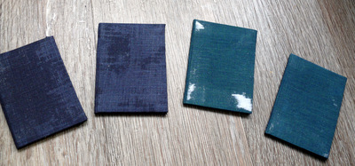 Vier A6 Bücher liegen nebeneinander. Zwei davon sind dunkelblau, zwei dunkelgrün.